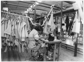 Interior de uma fábrica de confecção: mulher a coser à máquina