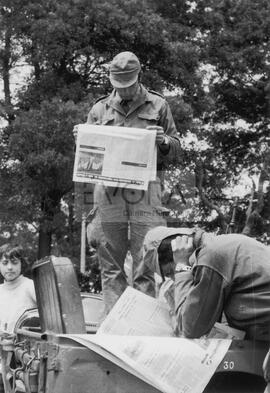 Militares a ler jornal em cima de um jipe